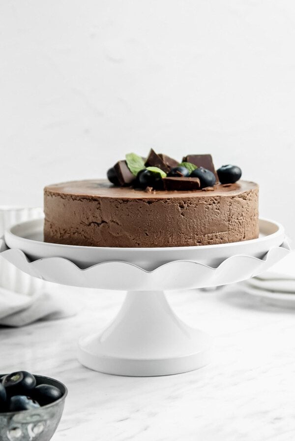 A chocolate cake topped with a few blueberries on a decorative cake stand.