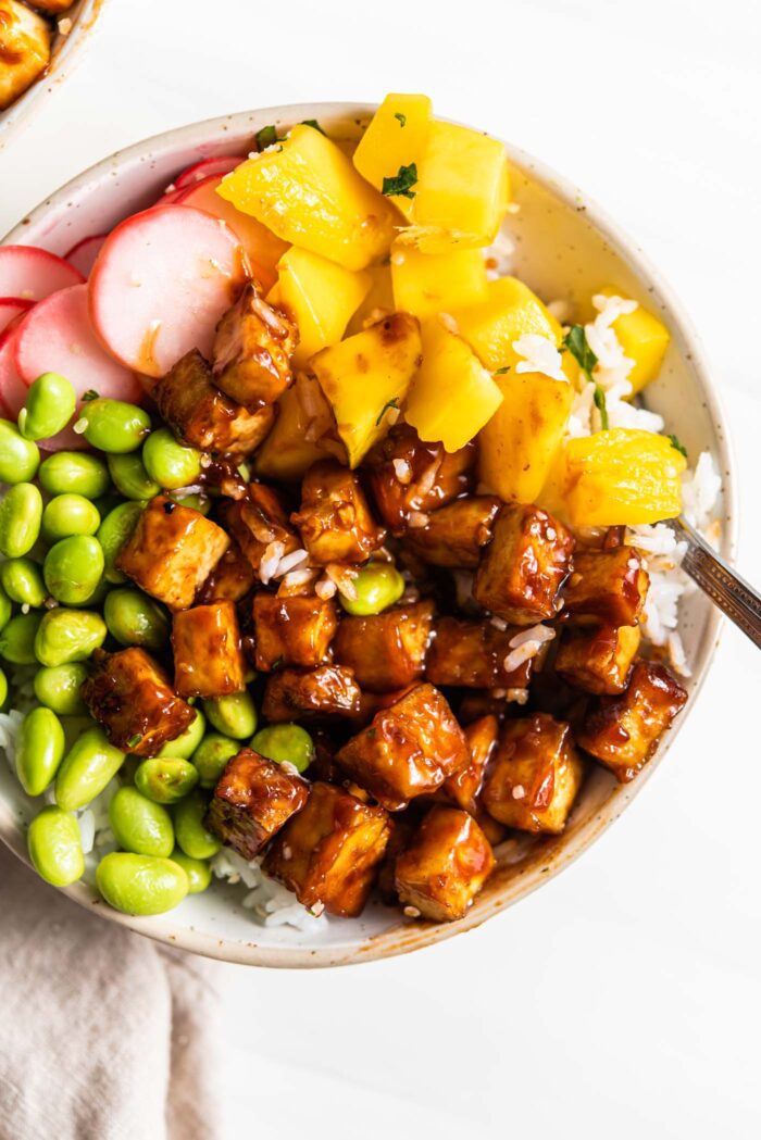 Tofu cubes in sauce in a bowl with edamame and mango.