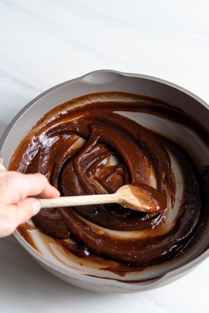 Thick brown sauce being stirred in a pan with wooden spoon.