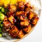 Close up of sweet and spicy tofu in a bowl with rice, mango and edamame.