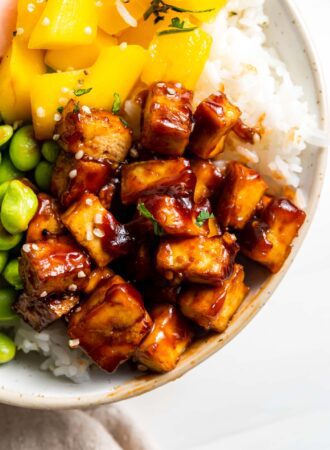 Close up of sweet and spicy tofu in a bowl with rice, mango and edamame.