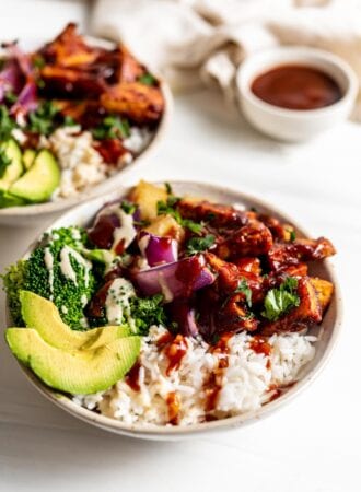 Two dinner bowls with rice, bbq tofu, avocado, broccoli, pineapple and roasted red onion.