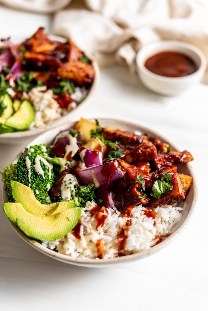 Two dinner bowls with rice, bbq tofu, avocado, broccoli, pineapple and roasted red onion.