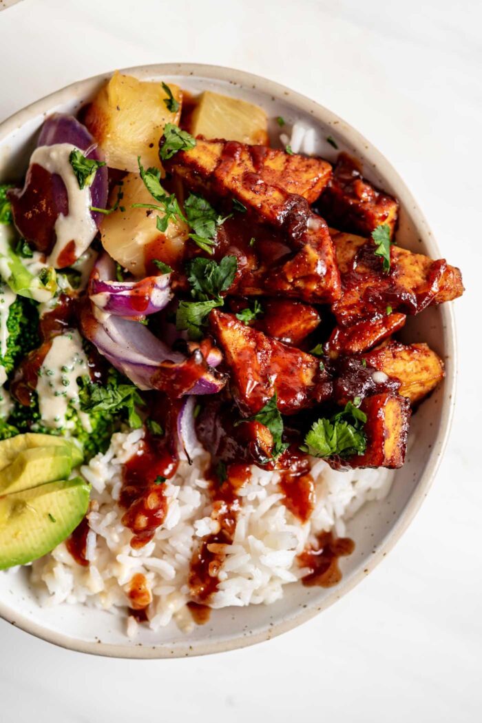 Close up overhead view of a bowl of rice, bbq tofu, avocado, red onion and pineapple.