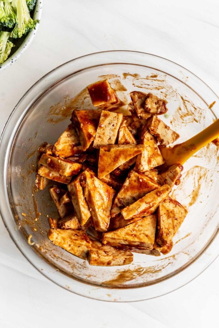 Tofu cut into triangles in a bowl with bbq sauce.