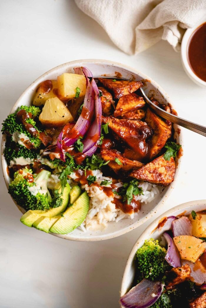 Overhead view of a bowl of rice, bbq tofu, avocado, red onion and pineapple.