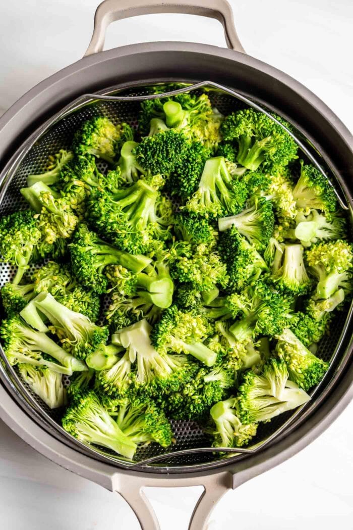 Steamed broccoli in a steamer basket in a pan.