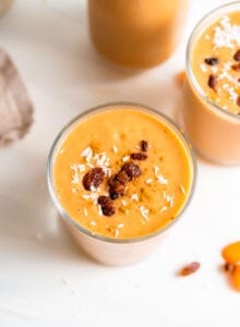 Creamy carrot smoothie in a glass topped with a few raisins.