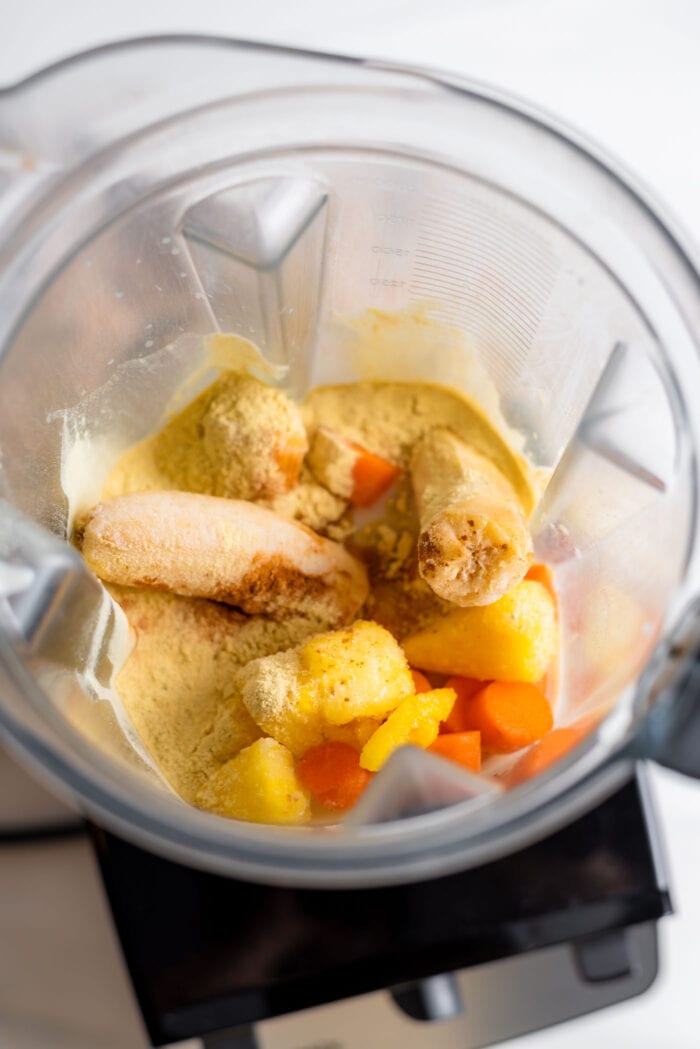 Banana, pineapple carrot and protein powder in a blender container.