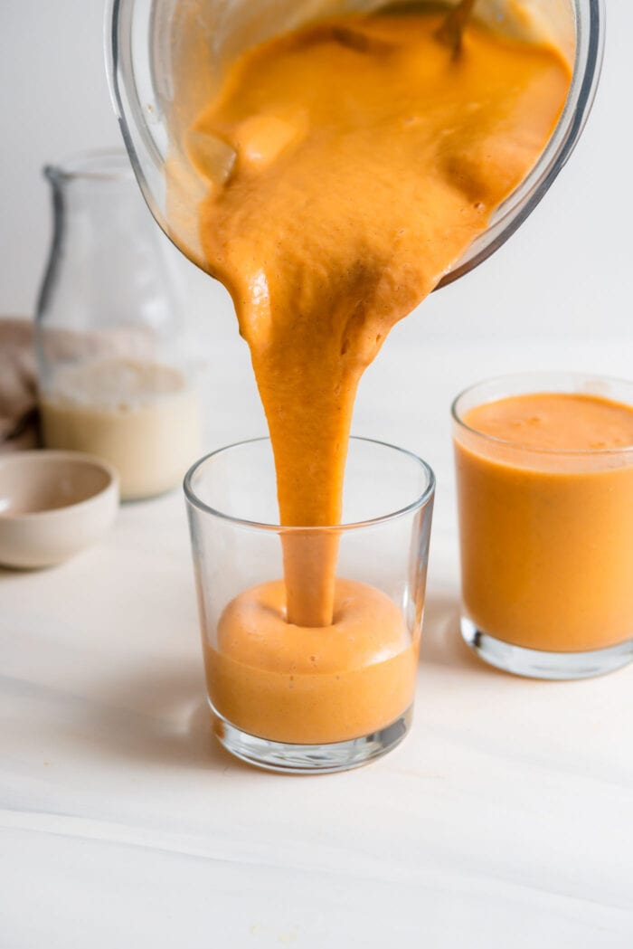 Pouring a thick carrot smoothie from a blender into a glass.