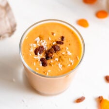 Creamy carrot smoothie in a glass topped with a few raisins.