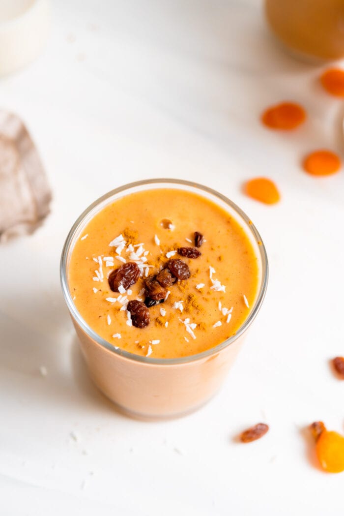 Creamy carrot smoothie in a glass topped with a few raisins.