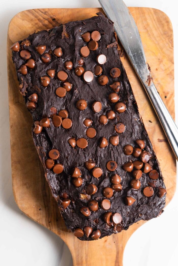 A loaf pan-sized tray of chocolate chip brownies on a cutting board with a knife.