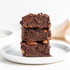 Stack of 3 chocolate brownies on a small white plate.