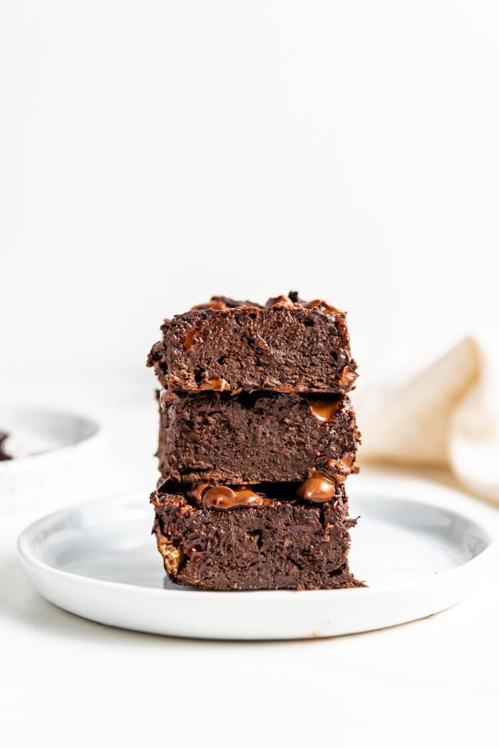 Stack of 3 chocolate brownies on a small white plate.