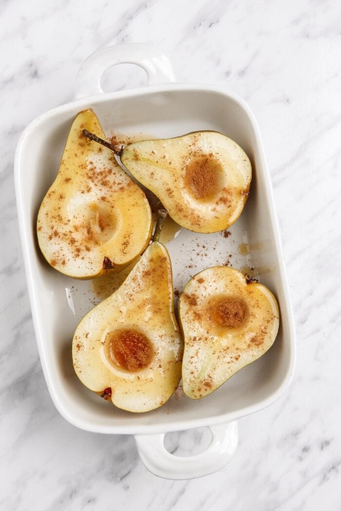 Spiced open pears in a baking dish drizzled in maple syrup and cinnamon