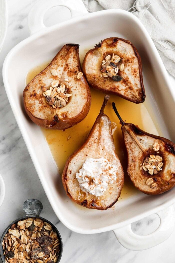 Baked pears topped with maple syrup and whipped cream in a baking dish.