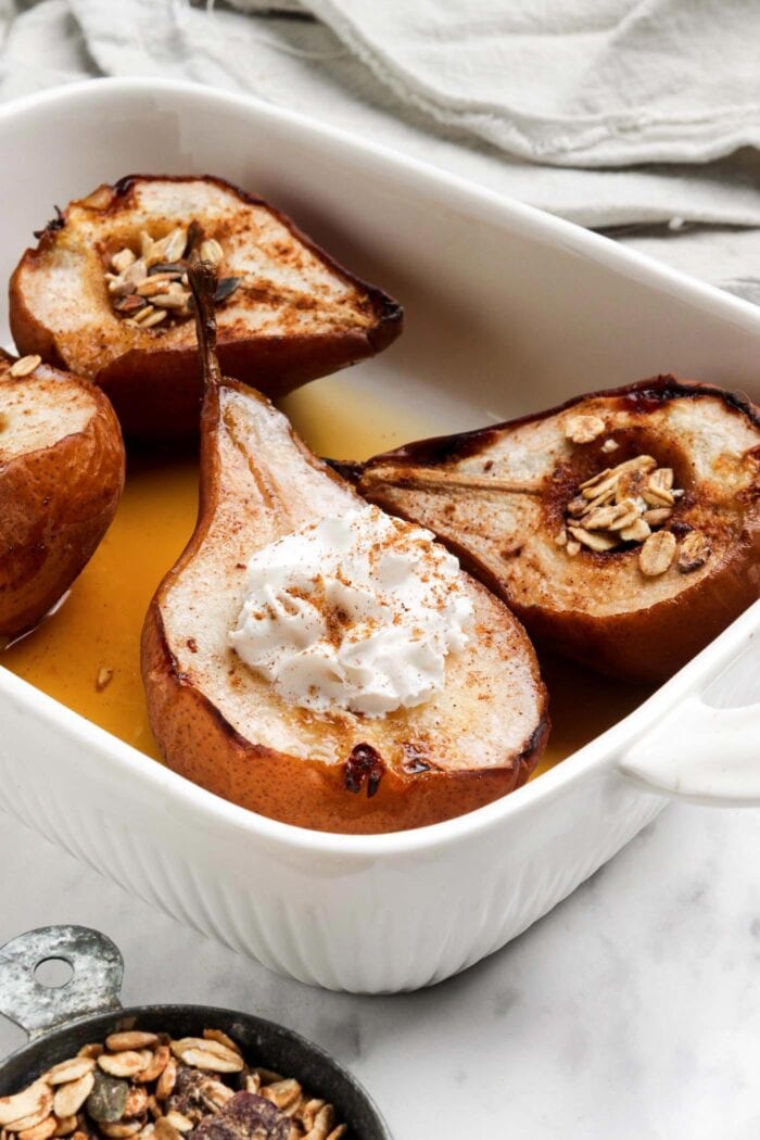 4 halves of baked pears topped with maple syrup and whipped cream in a baking dish.