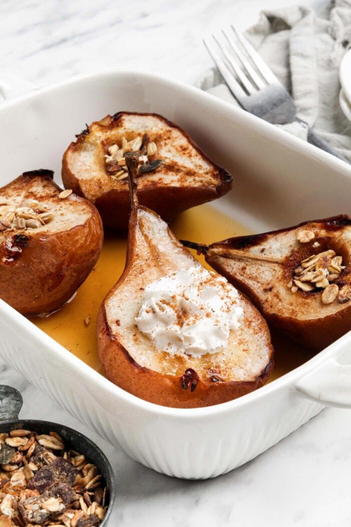 4 halves of baked pears topped with maple syrup and whipped cream in a baking dish.