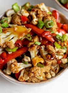 Bowl of cauliflower kung pao topped with chopped green onions and cashews.