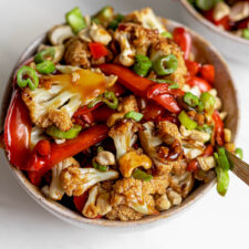 Bowl of cauliflower kung pao topped with chopped green onions and cashews.