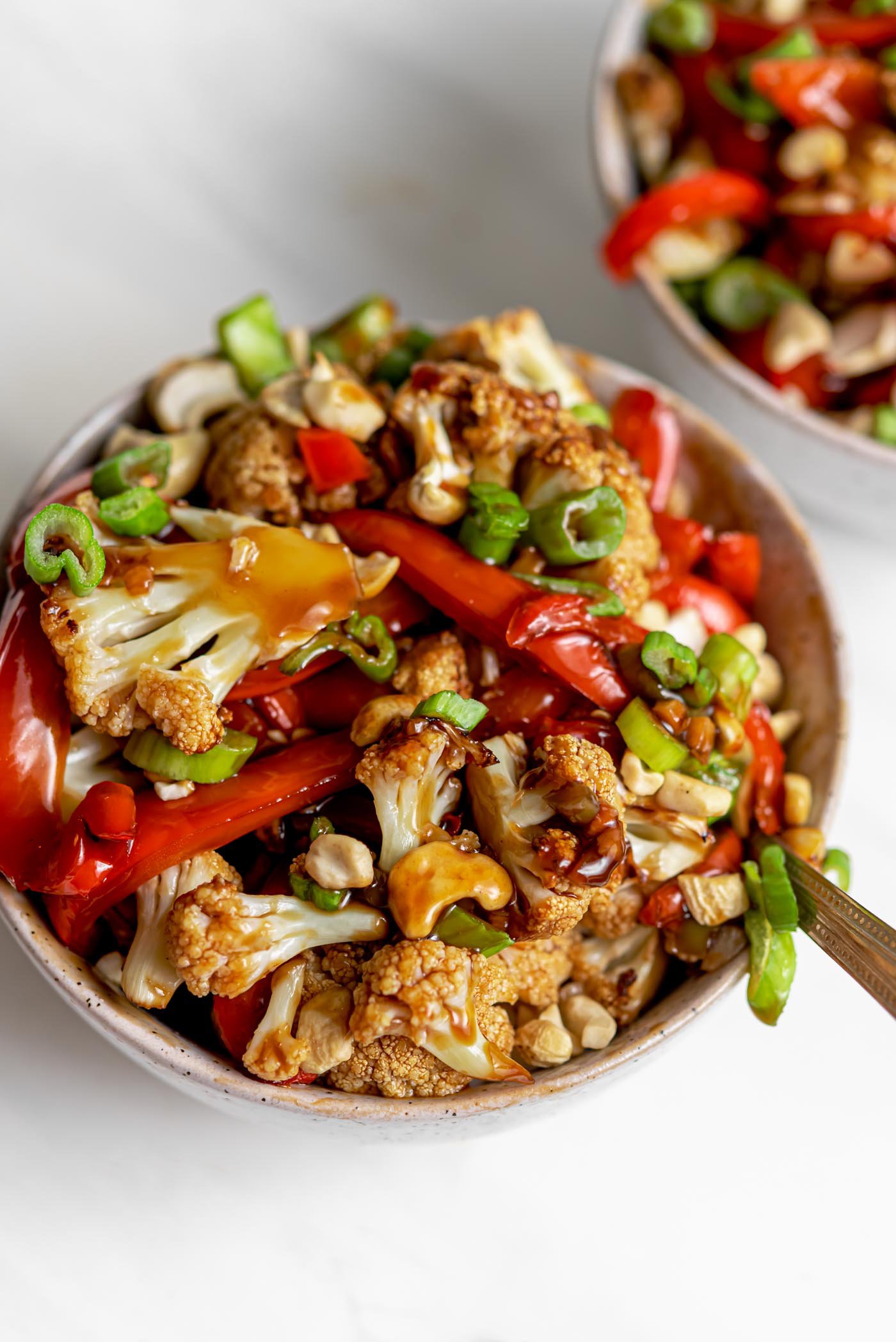 Two bowls of cauliflower kung pao topped with chopped green onions and cashews.