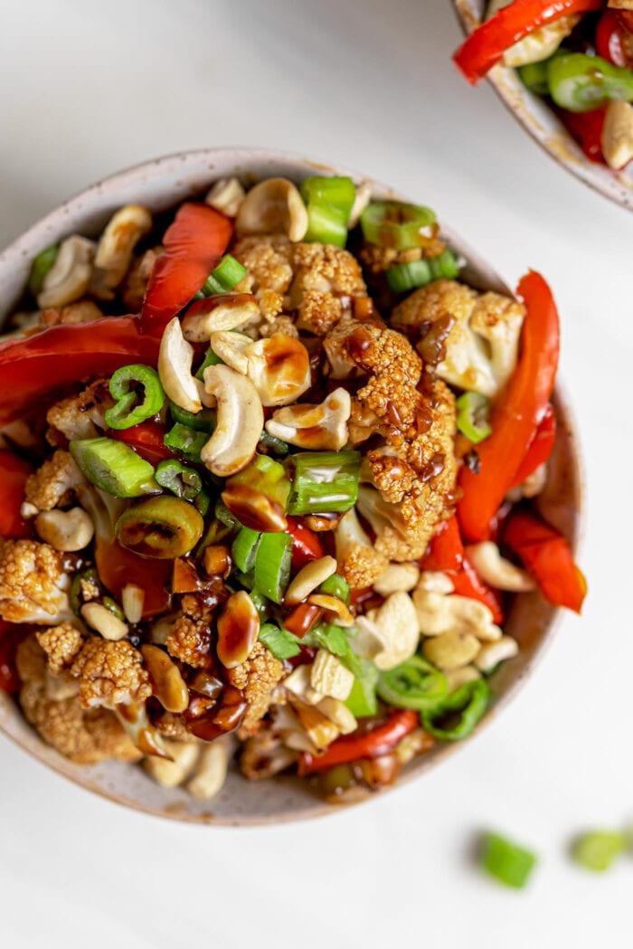 Overhead view of a bowl of kung pao cauliflower with bell peppers, green onion and cashews