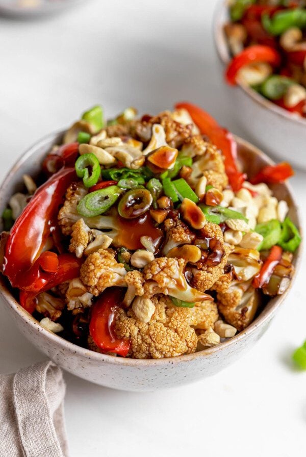 Bowl of cauliflower kung pao topped with chopped green onions and cashews.