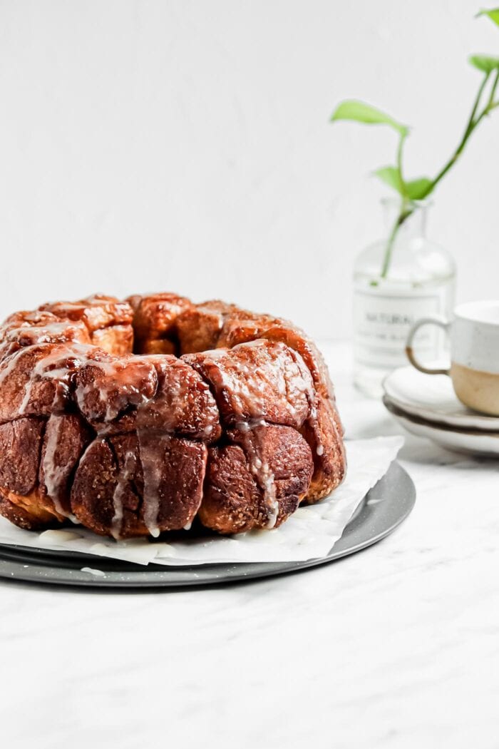 Monkey pull-apart bread on a plate with a cup of coffee and vase in the background.