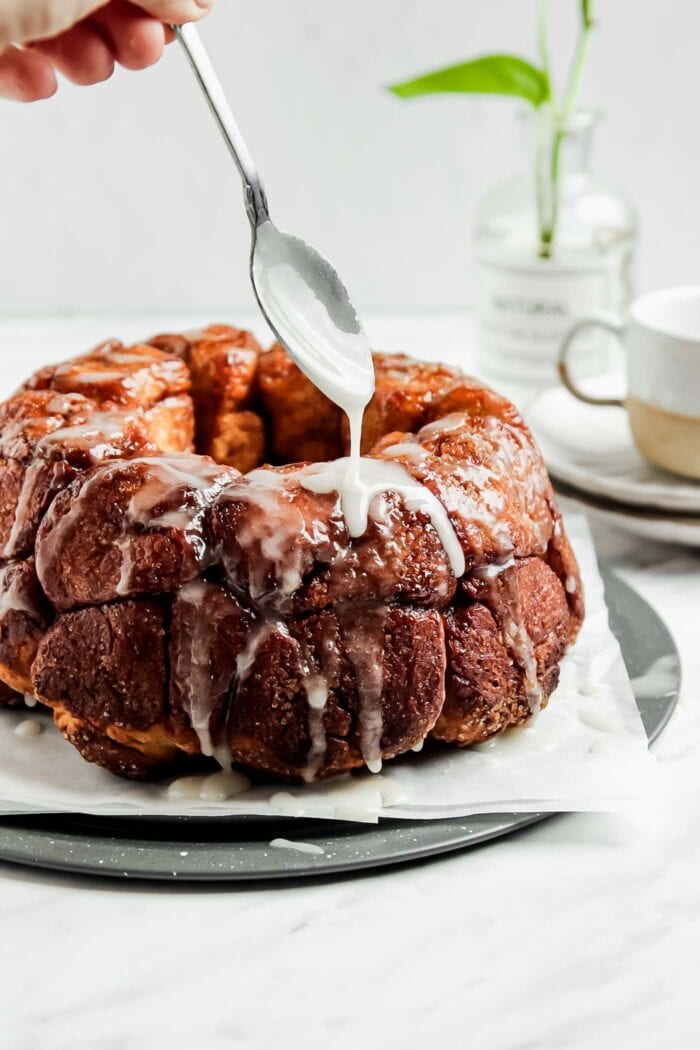Spoon drizzling icing over a monkey pull-apart bread on a plate.