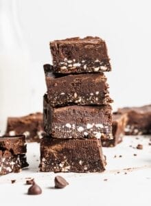 Stack of 4 triple layered chocolate squares with a few chocolate chips scattered around and a jar of milk in the background.