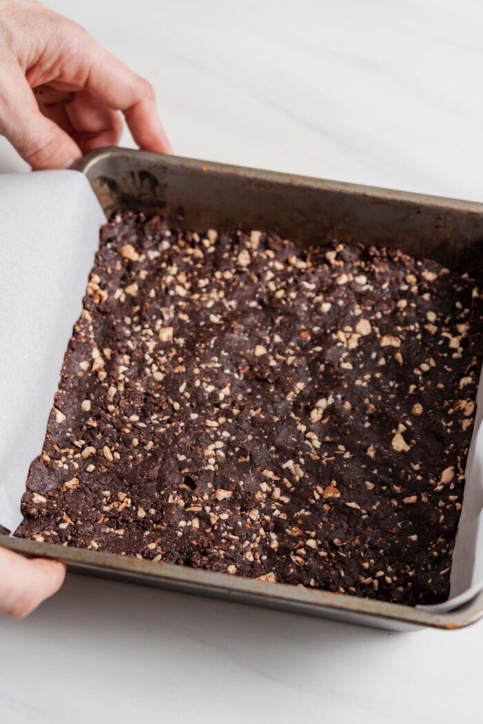 No-bake chocolate cashew bars pressed into a square baking pan lined with parchment paper.