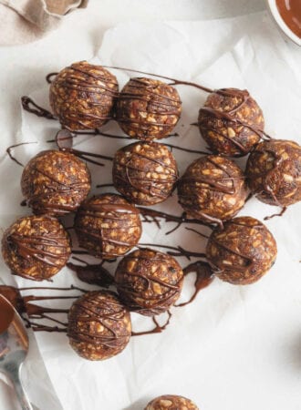 Overhead view of a number of no-bake energy balls drizzled in chocolate on a piece of parchment paper.