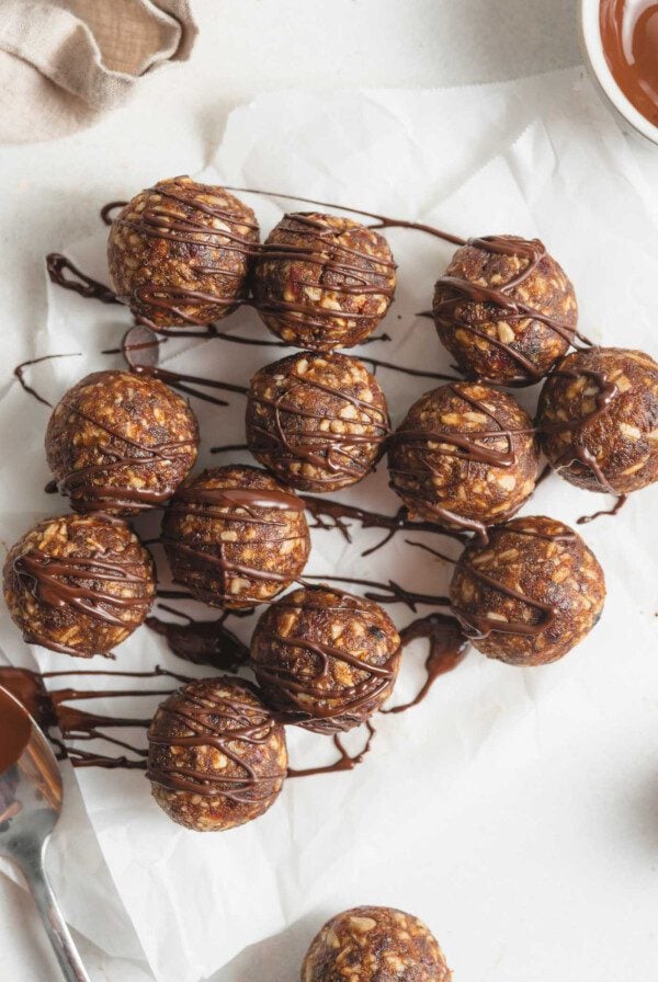 A number of no-bake energy balls drizzled in chocolate on a piece of parchment paper.