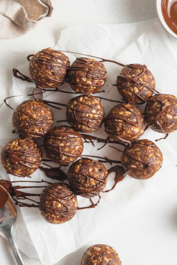 Overhead view of a number of no-bake energy balls drizzled in chocolate on a piece of parchment paper.