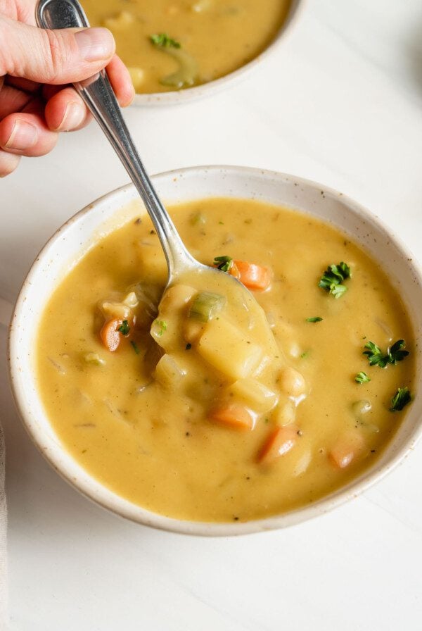 Hand using a spoon to take a spoonful of vegan chickpea soup from a bowl.