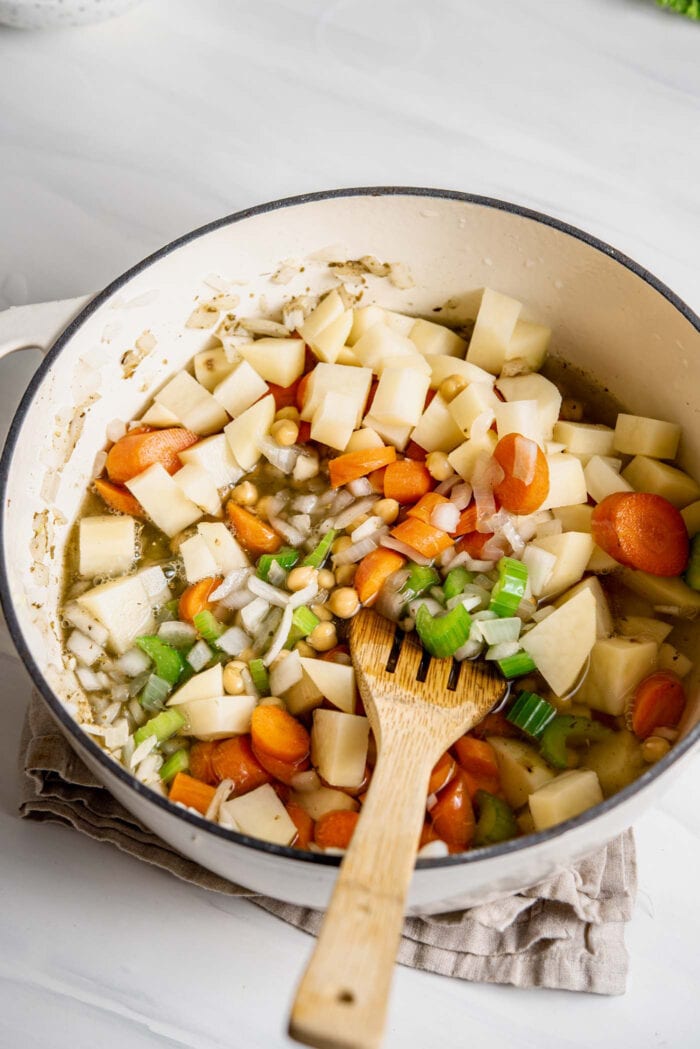 Potato, celery, carrots and chickpeas cooking in broth in a large soup pot.