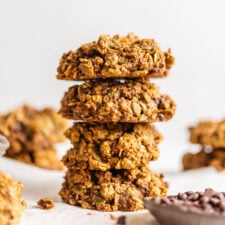 Stack of 4 sweet potato cookies with a small dish of chocolate chips in foreground and more cookies in background.