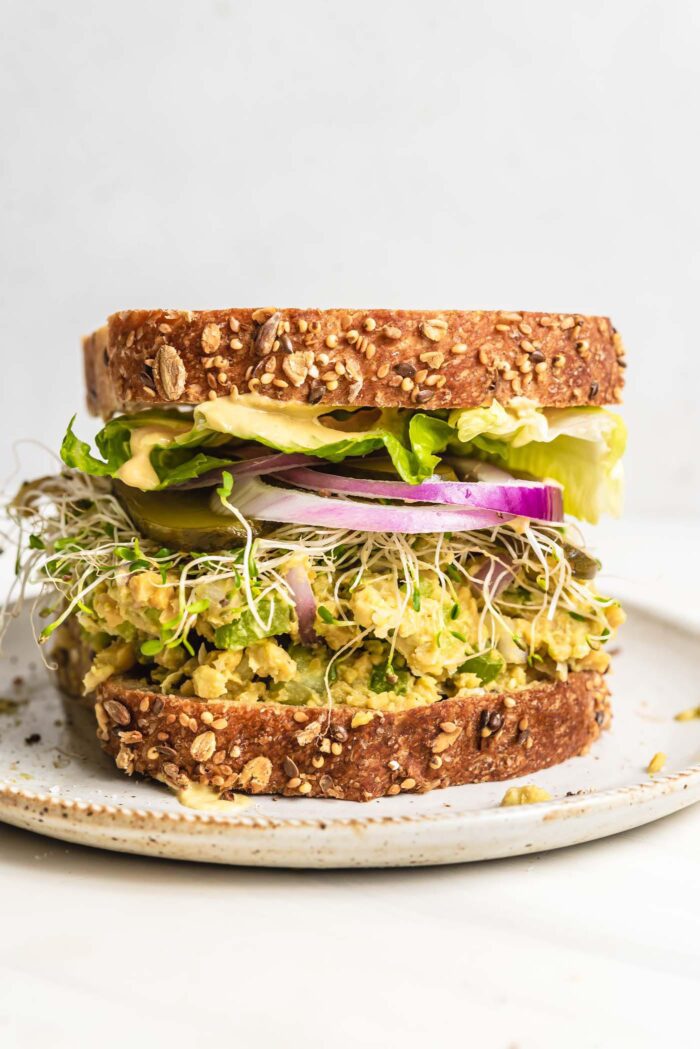 Close up view of a chickpea salad sandwich with onion, lettuce and sprouts.