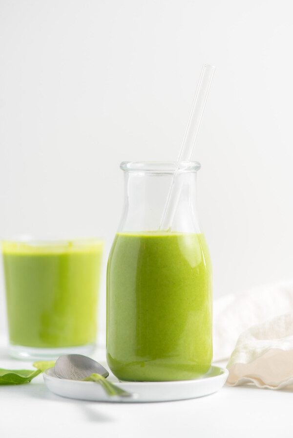 Green smoothie in a jar with another smoothie in the background.