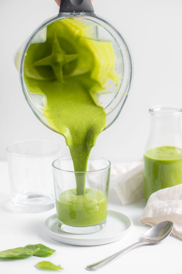Pouring a green smoothie from a blender into a glass.