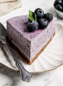 Slice of blueberry cheesecake on a small plate with a spoon.