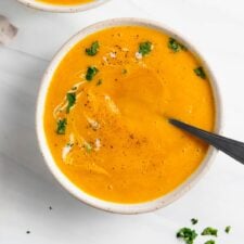 Overhead view of two bowls of butternut squash soup with spoons in them.