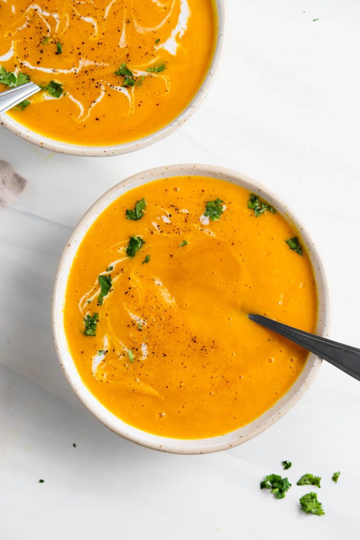 Overhead view of two bowls of butternut squash soup with spoons in them.
