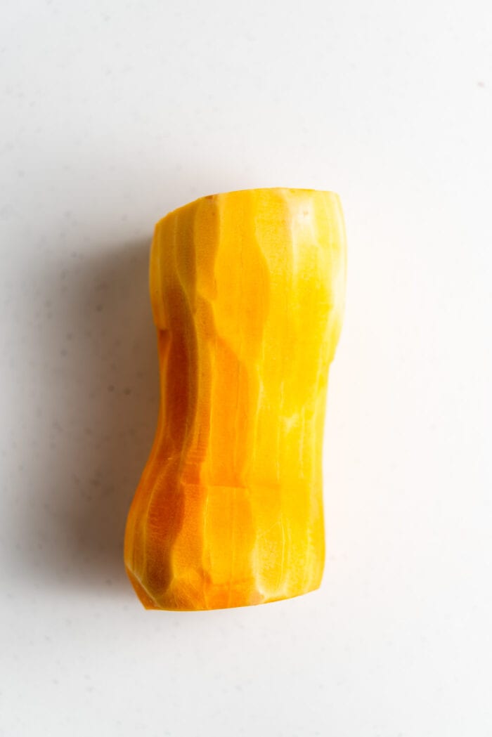 A peeled butternut squash with the top and bottom cut off.