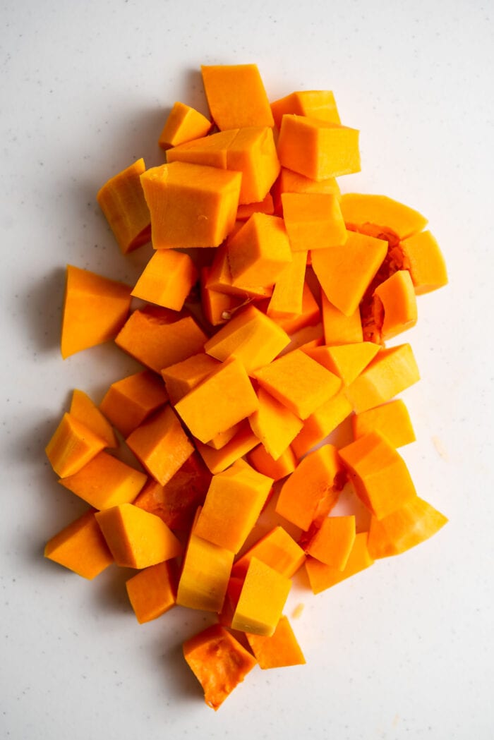 A pile of peeled and cubed butternut squash on a cutting board. 