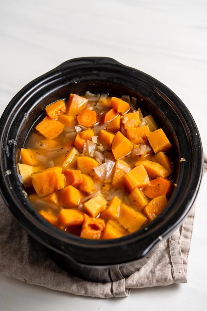 Chunks of butternut squash and onions cooking in a slow cooker.