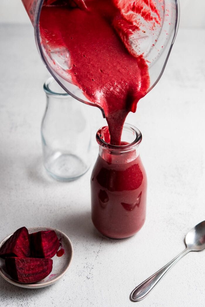 Pouring a beet smoothie from a blender into a jar.