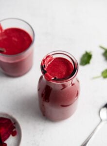 Beet smoothie in a jar with another small glass behind it and a small dish of chopped beets beside it.