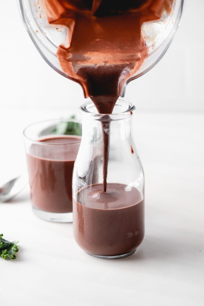 Pouring a chocolate smoothie from a blender into a glass jar.